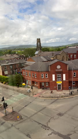 Vertical video. Panning shot of part of Bury town centre through window. Part of bus station behind crossroad, wind farm on hills in the background, high angle view looking through window.