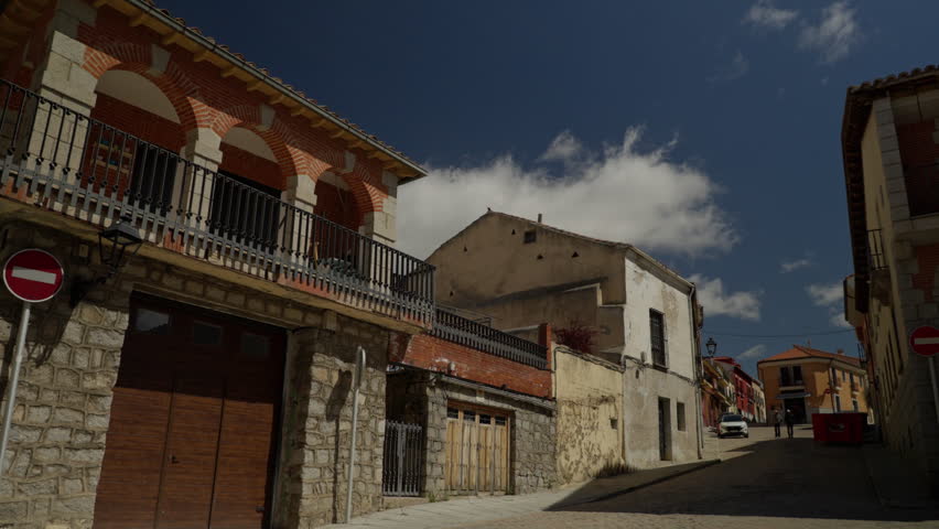 Historic street featuring traditional architecture, stone walls, balconies, and a no entry sign under a bright blue sky