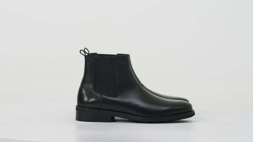 Black leather chelsea boots rotating on a turntable isolated on a white background, studio shot of classic footwear