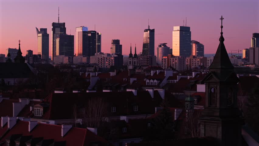 Panoramic view of Warsaw city during purple dusk. Cinematic footage shows transition from traditional rooftops and church domes to contemporary high rise architecture under colorful sky.