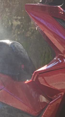 Close up of washing a red scooter with a high pressure water jet focusing on the front wheel and fairings