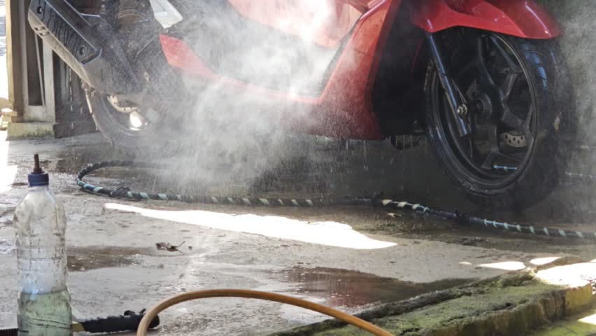 Close up of washing a red scooter with a high pressure water jet focusing on the front wheel and fairings