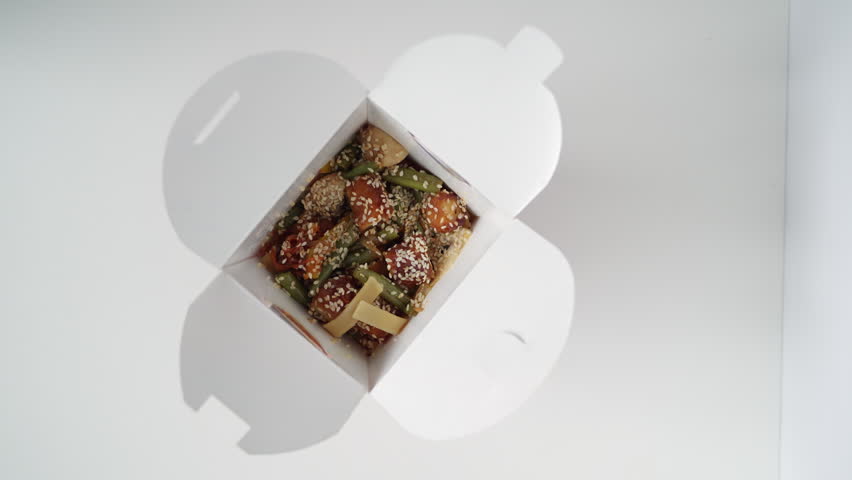Chinese wok noodles with teriyaki chicken and sesame seeds in a takeaway box isolated on a white background