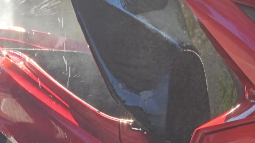 Close up view of a person cleaning a red motorcycle using a high pressure water gun to remove dirt