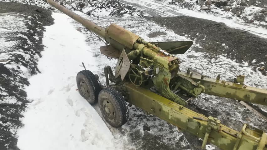 A stationary military field gun positioned in a snowy quarry with its long barrel and breech mechanism prepared for use during a cold winter day