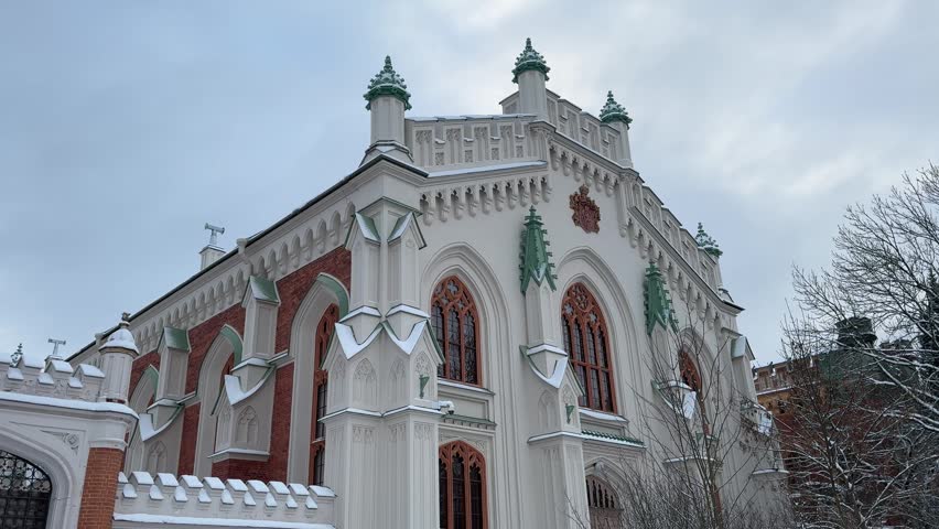 White Gothic church with decorative spires and red brick details standing in a snowy winter park.