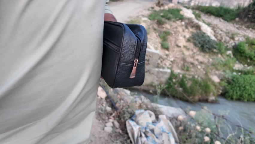 Black PU leather men’s clutch with wristlet strap and zippered pocket outdoors in nature.