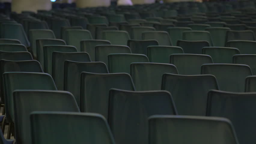 Dense rows of empty green plastic chairs closely arranged in symmetrical pattern inside large hall prepared for public gathering or conference