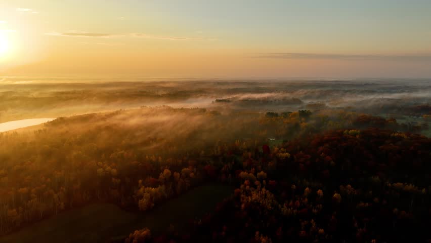 Beautiful dawn aerial shot of sunlight shining thought the trees and low fog in Minnesota in the autumn. Trees are turning their fall colors