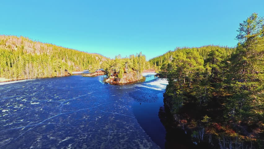 Drone aerial footage of a forested peninsula surrounded by dark open water and spring lake ice. Evergreen trees, reflections and peaceful Nordic wilderness scenery viewed from above.