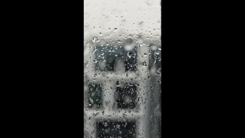 Raindrops on window glass with blurred urban building in background.