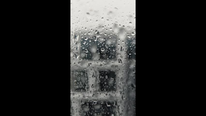 Raindrops on window glass with blurred urban building in background.