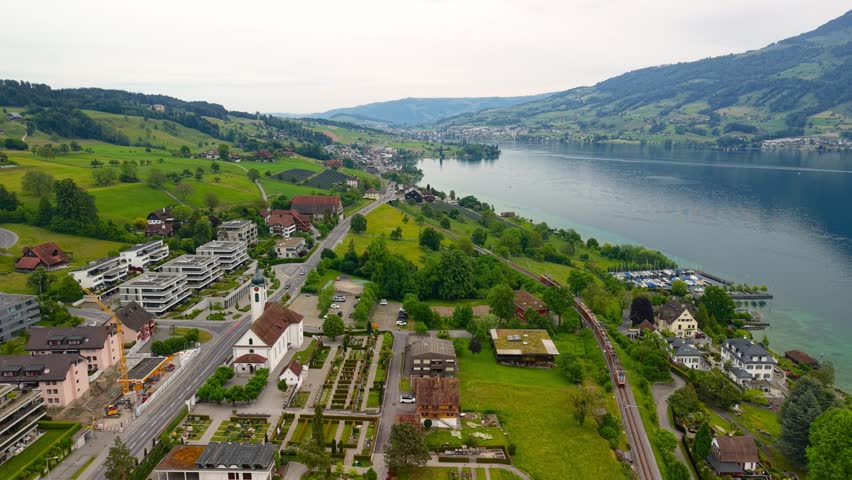 Aerial view of the Swiss village of Meggen on the shore of Lake  Lucerne with a moving passenger train.