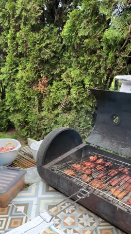 Close up of delicious meat slices roasting on a metal wire rack over hot charcoals with steam rising up on a backyard