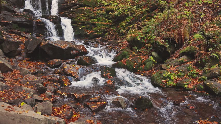 Waterfall falling down mountain slope in autumn forest