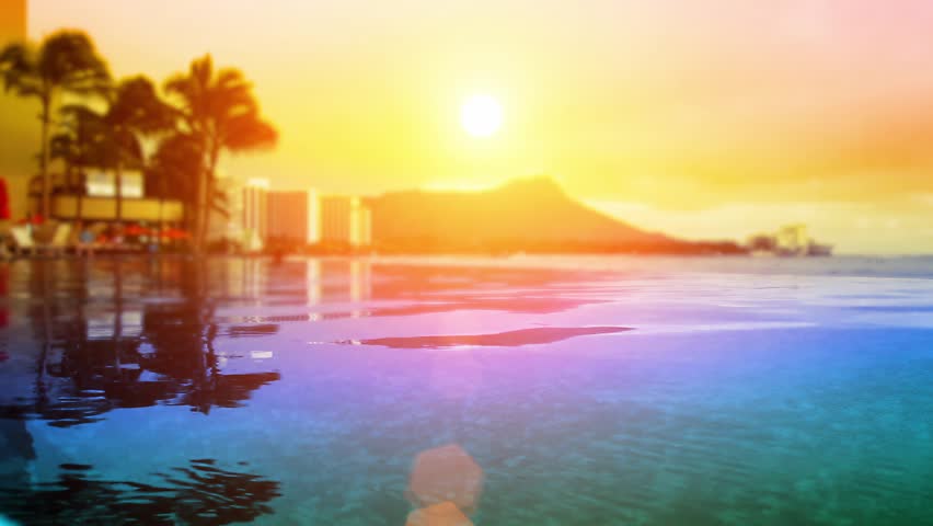 Luxurious looping 4K footage of a breathtaking Hawaiian sunset over Waikiki. Iconic Diamond Head mountain and palm trees perfectly reflected in a calm resort infinity pool. Warm golden tones, vibrant colors, and serene tropical ambiance – ideal for travel promos, hotel ads, relaxation, and luxury content.