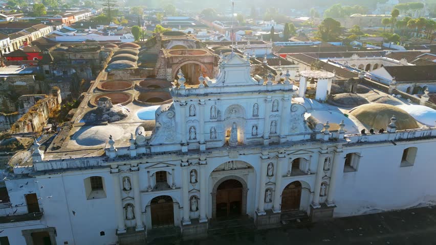 Aerial view of ancient cathedral in antigua guatemala city with white facade and birds flying fast.