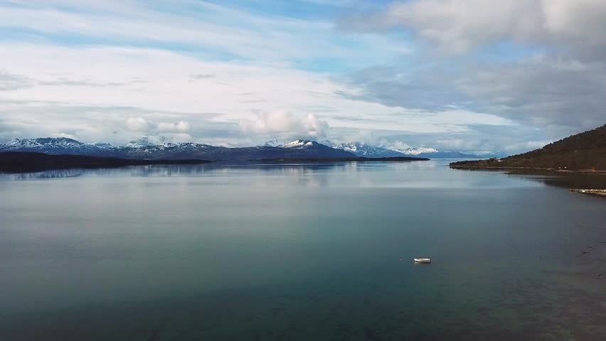 A wide view shows islands surrounded by water with mountains and trees in the background. The sun is shining and the sky is mostly clear. This area is located in Norway.