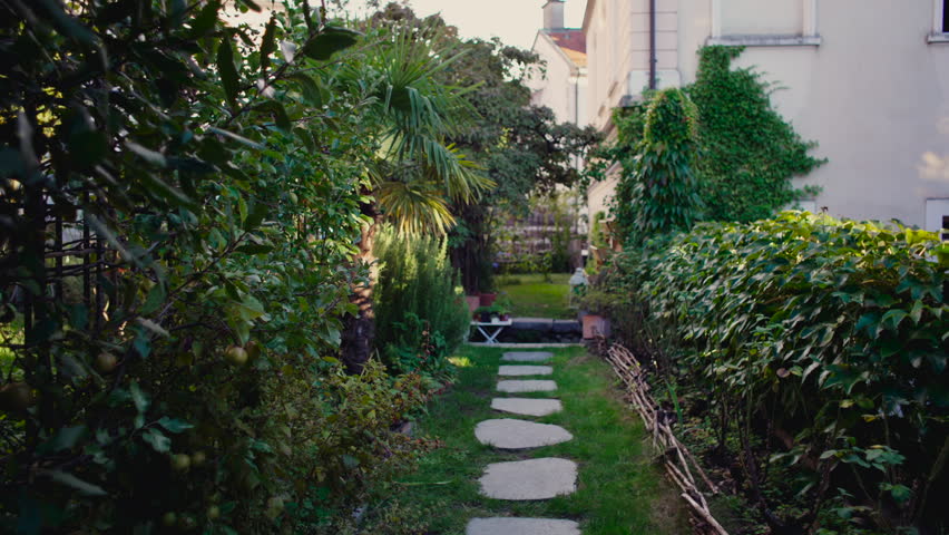 Narrow garden path lined with dense plants and stone steps leading toward small sitting area, showing tranquil outdoor environment and relaxed natural home landscape
