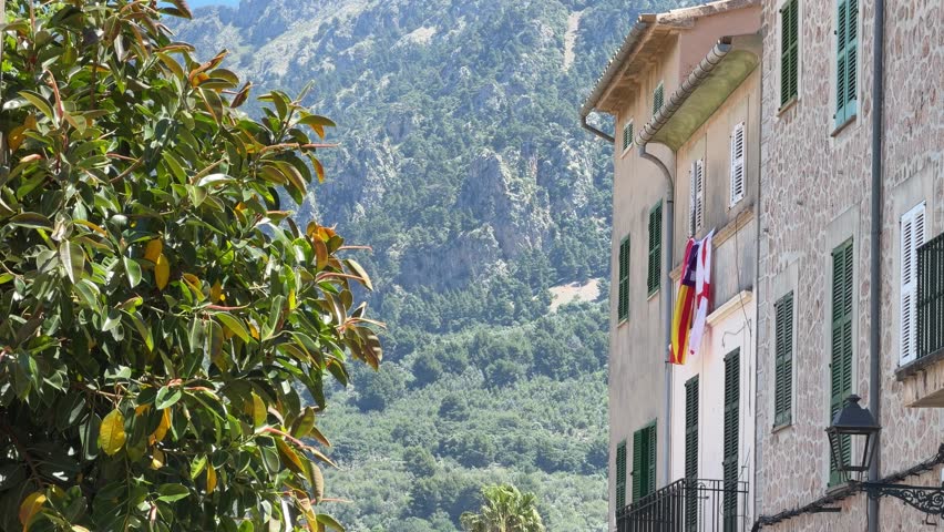 Charming street in Soller, Mallorca, framed by traditional stone buildings and lush greenery, with the dramatic Tramuntana mountains rising in the background.