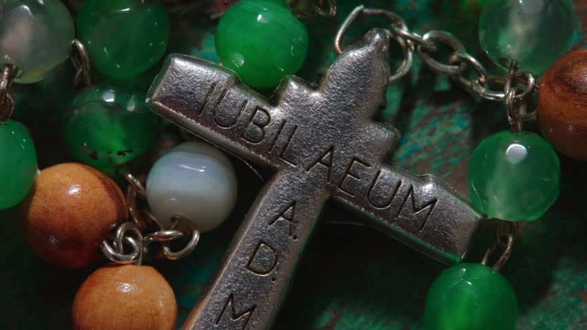 Close detail of rosary necklace with green and wooden beads, metal chain, and cross pendant reading "Jubilee Year 2025" in Latin, spiritual accessory used for meditation worship and reflection