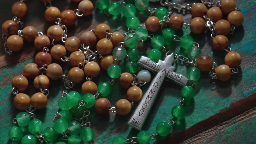 Macro composition of Christian rosary chain with detailed crucifix reading "Jubilee Year 2025" in Latin, resting across textured background, sacred symbol connected to meditation worship and church life