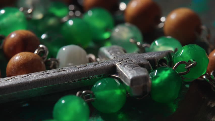 Angled close view of Catholic rosary with metal cross and polished beads resting on textured wood, sacred object associated with meditation reflection and church tradition