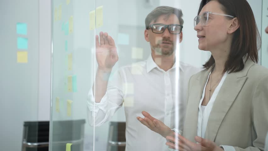 Business colleagues collaborating on a glass board in an office, discussing strategy, sharing ideas, and brainstorming during a productive meeting for project development
