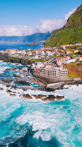 Aerial drone view of Porto Moniz coastal town with volcanic shoreline and powerful Atlantic Ocean waves during bright daytime conditions