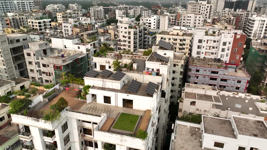 Aerial view orbiting a residential building with rooftop gardens and solar panels, revealing the dense and overpopulated urban cityscape of dhaka, the capital city of bangladesh