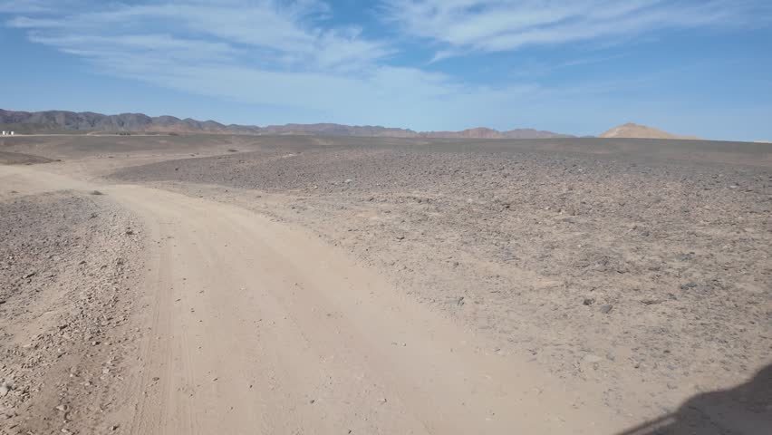 Pov from a vehicle driving on a rough dirt road through the arid and rocky desert landscape of marsa alam, egypt, with mountains visible on the horizon under a clear blue sky