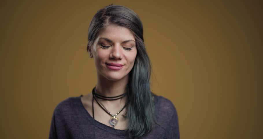 Portrait of a cheerful young woman with a subtle smile, featuring her fashionable hairstyle and casual attire, set against a mustard yellow background.