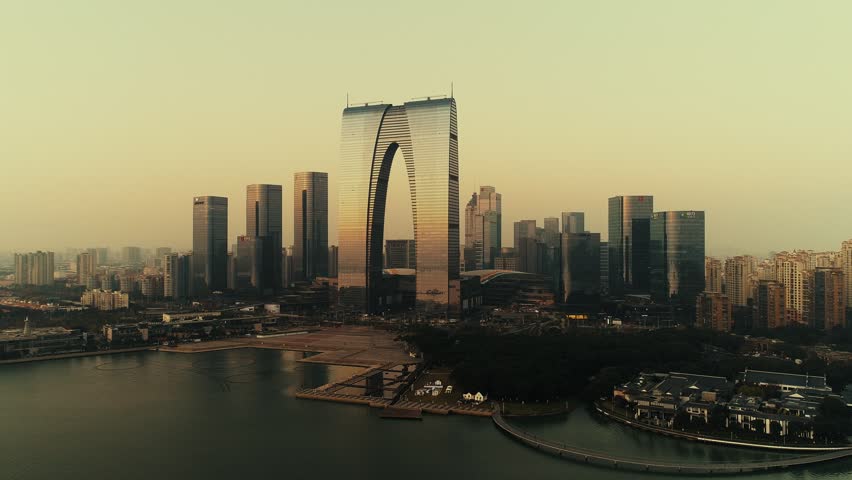 Suzhou. Aerial view of a cityscape during what appears to be either dawn or dusk, with a hazy sky and a calm body of water in the foreground.
