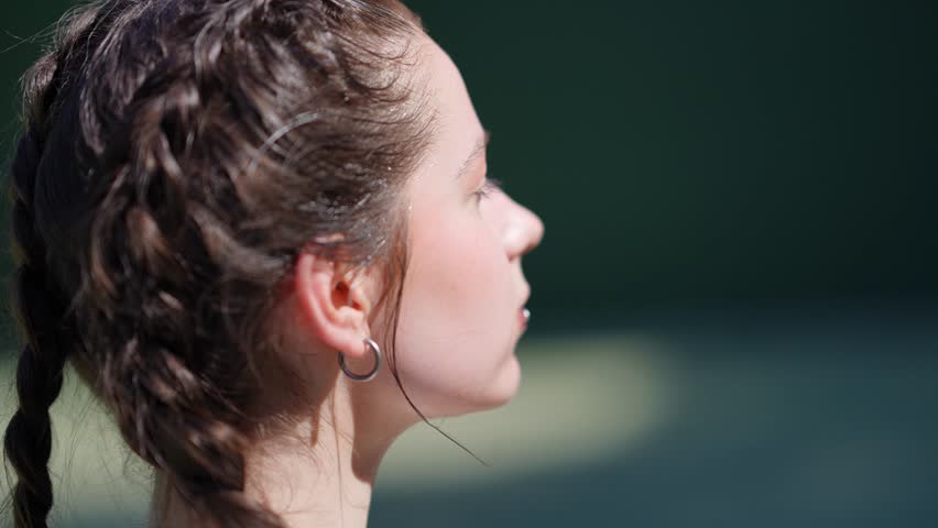 Serene young woman with braided hair basking in the sun. She gently applies sunscreen to her face, enjoying a warm, peaceful outdoor moment
