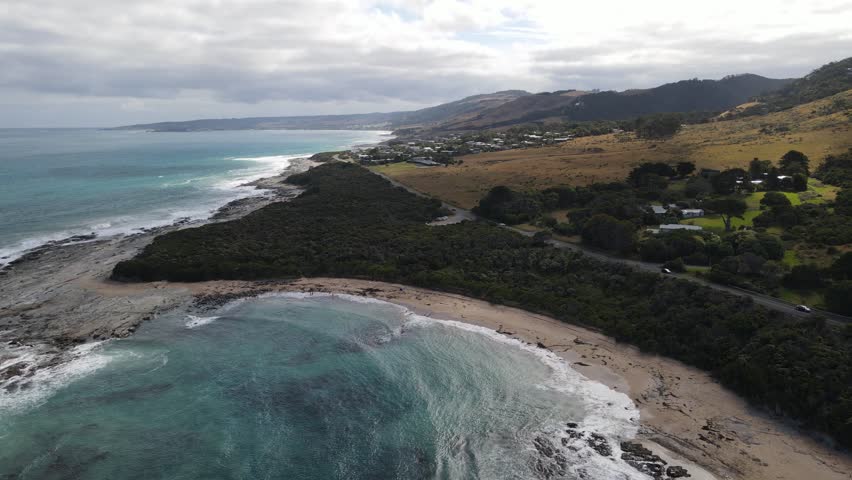 Scenic panoramic aerial view of a car driving along the famous Great Ocean Road next to the ocean coast and green hills, Victoria, Australia