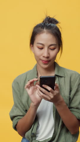 Vertical Screen : Asia youth isolated lady on empty space play smartphone feel boring thinking send message emotional happy smile looking at camera on yellow background. Mock up copy space concept.