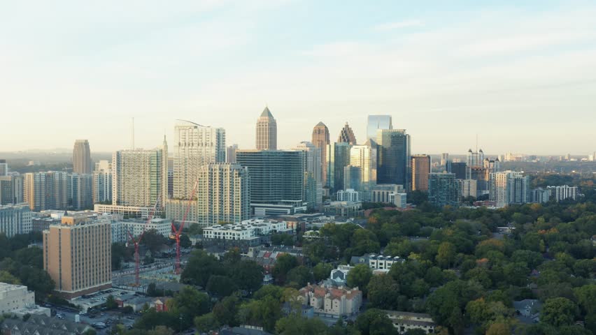 Aerial view of Atlanta skyline skyscrapers, dynamic drone movement over cityscape, urban sprawl, trees in golden hour light, city skyline establishing shot footage.