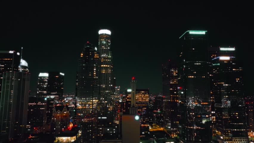View of the Los Angeles skyline at night shows illuminated skyscrapers and buildings in the financial district. City lights create a lively urban landscape.