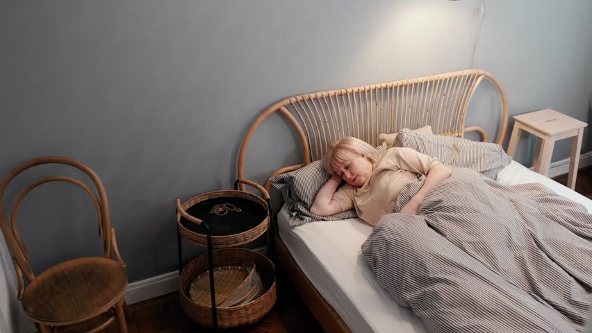 Grandma is sleeping in bed while Grandpa carries the cups to the table and sits down, then kisses her