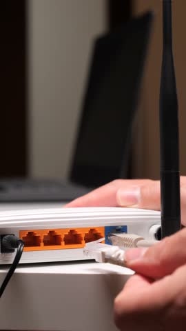 Vertical video person connecting an ethernet cable to the lan port of a white wireless router, symbolizing modern connectivity, home networking, and internet access for digital communication