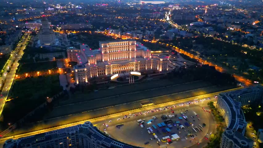 Cinematic high angle night view of the illuminated Palace of the Parliament in Bucharest, Romania. Iconic architectural landmark surrounded by city lights.