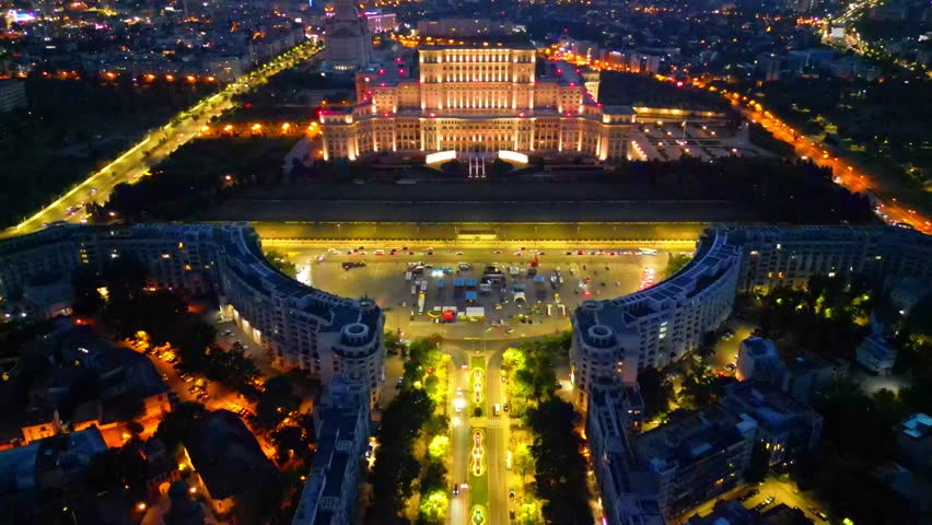 Cinematic high angle night view of the illuminated Palace of the Parliament in Bucharest, Romania. Iconic architectural landmark surrounded by city lights.