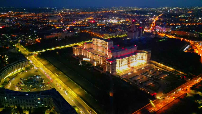 Cinematic high angle night view of the illuminated Palace of the Parliament in Bucharest, Romania. Iconic architectural landmark surrounded by city lights.