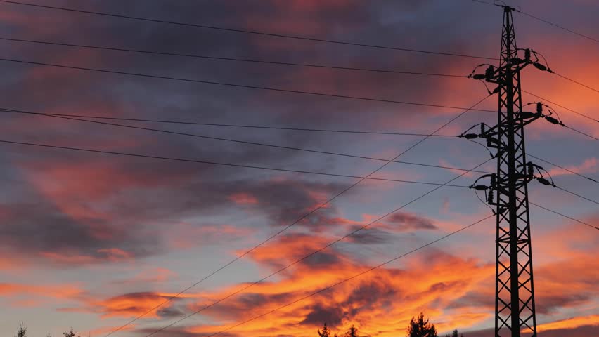 Electric Power Pylon Silhouette Against Vibrant Sunset Sky Over Winter Forest Landscape Background