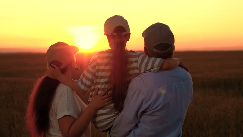 Happy farm family in field. People dreaming bright future. Father mother, child daughter, happily hugging sunset. Loving parents, little girl in arms, enjoying nature in wheat field sun. Parents girl