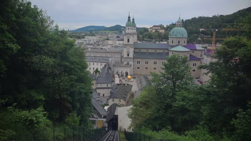Panoramic spring view of Salzburg rooftops and historic fortress complex framed by trees in Austria.