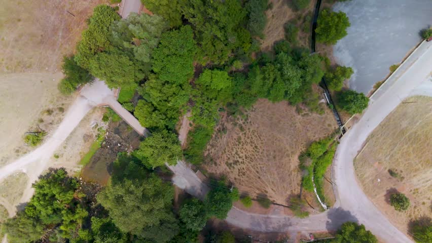 A top-down aerial drone shot reveals the limestone entrance of the Aggitis River Cave surrounded by a dense green forest canopy in Eastern Macedonia.