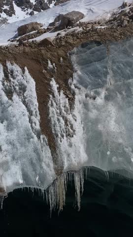 A person with trekking poles stands near an icy mountain crack surrounded by snowy slopes. Outdoor exploration