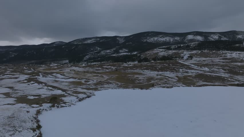 Aerial view of snowy steppe and rugged shoreline along Lake Baikal with mountain ridge and dark storm clouds, remote Siberian landscape in Russia