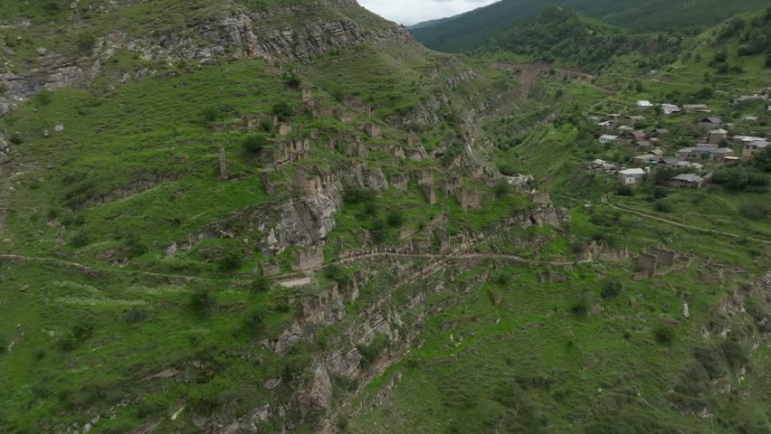 Drone footage of the abandoned stone aul of Kahib on a steep green mountainside, with terraced ruins and paths in the Caucasus, Dagestan, Russia